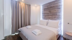 A modern bedroom with a wooden headboard, a bed with white linens, and a small bedside table.