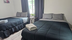 Ein Zimmer mit zwei Betten, jeweils mit dunkelblauer Bettdecke und Kissen, einem kleinen Tisch mit einer Pflanze und einem Fenster mit Vorhängen.