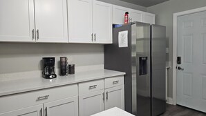 Eine Küche mit weißen Schränken, einem Edelstahl-Kühlschrank, einer Kaffeemaschine und einem Wasserspender.