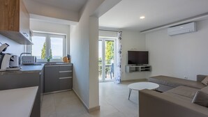 Uma cozinha moderna com forno embutido, área de refeições com mesa branca e dois sofás, e uma TV fixada na parede.