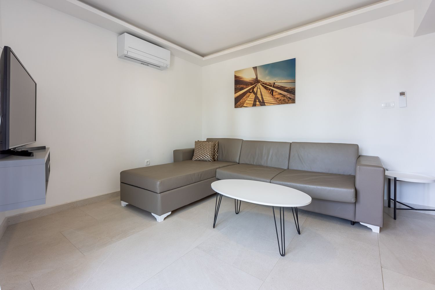 Un salon moderne avec un canapé d’angle, une table basse blanche et un téléviseur à écran plat.