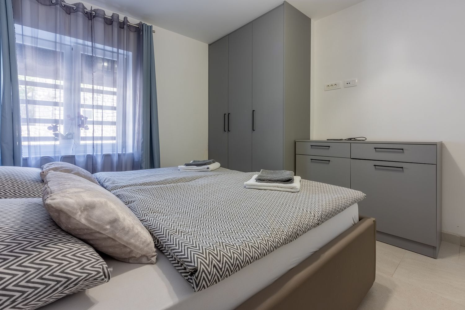 Ein modernes Schlafzimmer mit Bett, grauem Kleiderschrank und Schreibtisch.