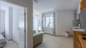Una habitación moderna y bien iluminada con una cama, una mesita con fruteros, una ventana con cortinas y un escritorio con computadora.