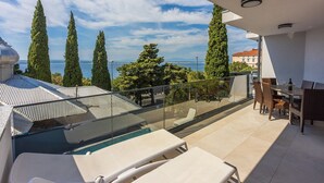 Un balcón con piscina, mobiliario exterior y vistas al mar y árboles.