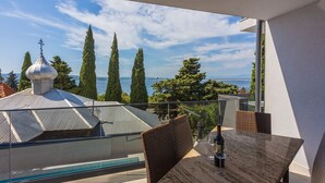 Un balcón con mesa y sillas, con vista a un cuerpo de agua y árboles.