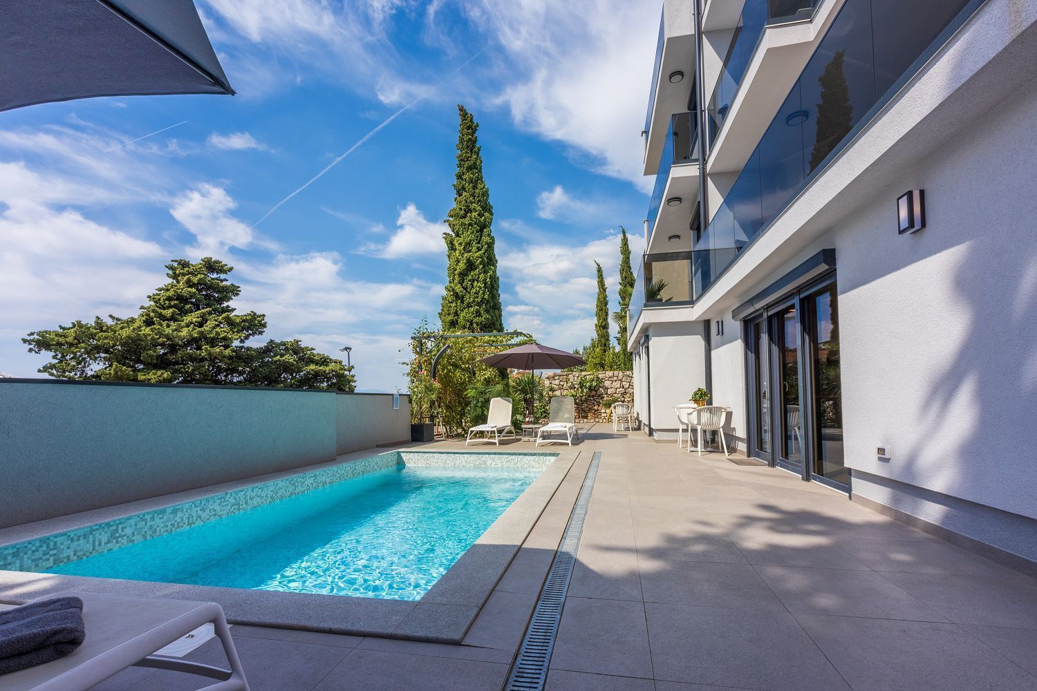 A modern outdoor pool area with a clear blue pool, lounge chairs, and a stone wall.