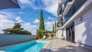 A modern outdoor pool area with a clear blue pool, lounge chairs, and a stone wall. - 500 metres beach with pool (Crikvenica)