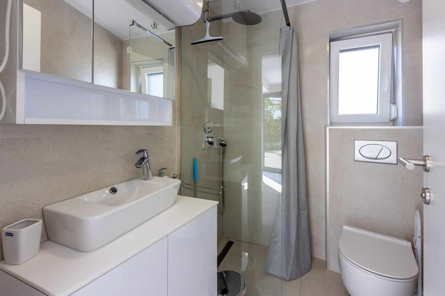 Une salle de bain moderne avec un lavabo blanc, un miroir, une douche et des toilettes.