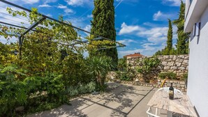 A patio area with a stone wall, a tall tree, and a table with a bottle and glasses. - 500 metres beach with pool (Crikvenica)