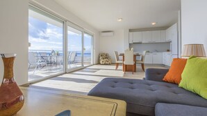 A modern living room with a sofa, a dining area with chairs, a kitchen, and a large sliding glass door leading to a balcony with a view of the sea. - 100 metres beach with sea view (Crikvenica)