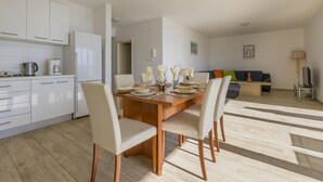 A modern kitchen with white cabinets, a dining table set for four, and a living area with a sofa and a coffee table. - 100 metres beach with sea view (Crikvenica)