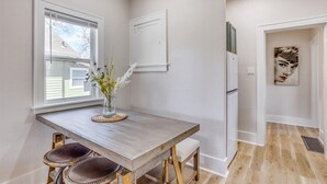 A modern kitchen with a wooden table, two stools, a vase with flowers, and a refrigerator. - Walk to Wesley! Pet Friendly + Fully Fenced Lot (Wichita)