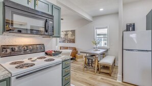 A modern kitchen with a white stove, a microwave, and a refrigerator. There is a wooden table with a bench, and a window with a view of the outside. - Walk to Wesley! Pet Friendly + Fully Fenced Lot (Wichita)