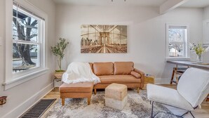 A living room with a brown sofa, a white chair, a coffee table, and a large painting on the wall. - Walk to Wesley! Pet Friendly + Fully Fenced Lot (Wichita)