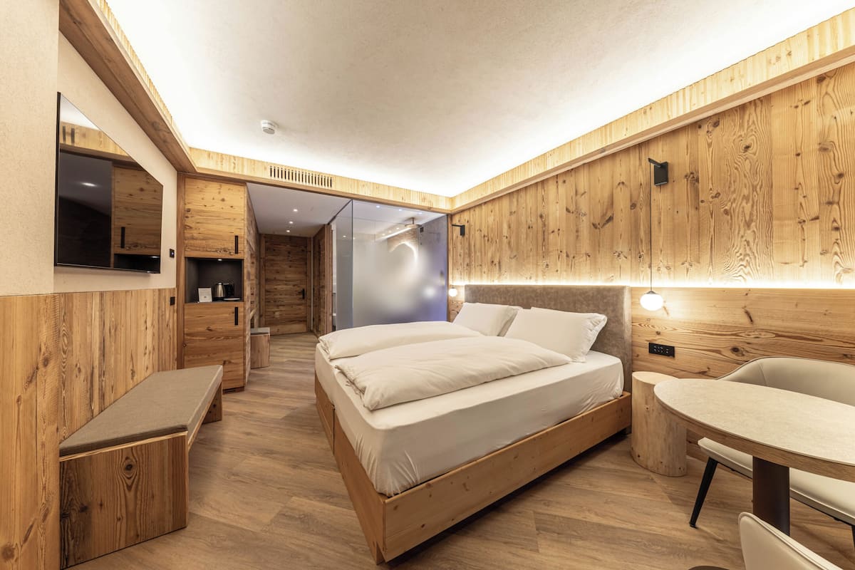 A modern bedroom with a wooden floor, a bed, a desk, and a mirror.