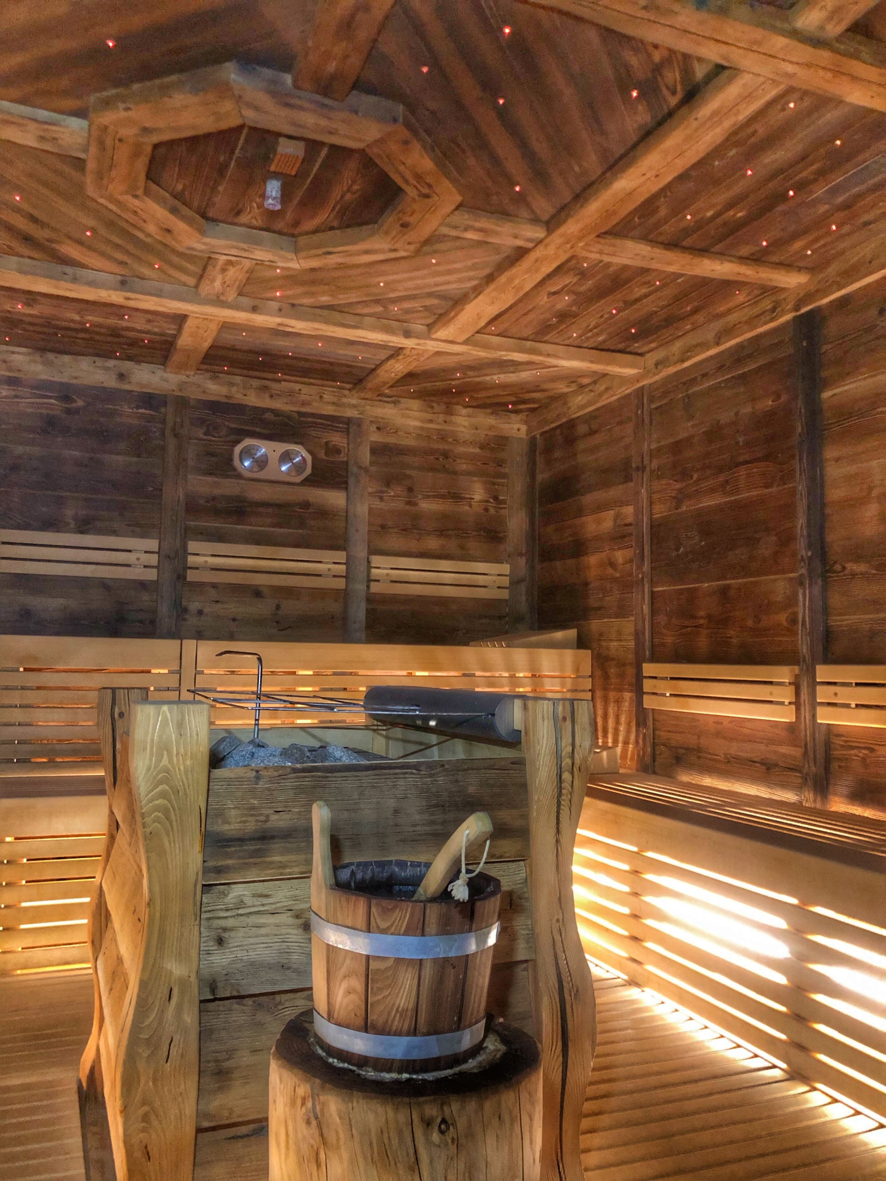 Uma sauna de madeira com um banco de madeira, um balde e uma parede de madeira com um relógio.