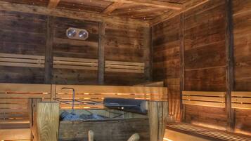 Uma sauna de madeira com um banco de madeira, um balde e uma parede de madeira com um relógio.