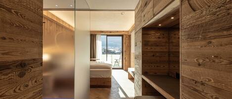 A modern interior with wooden walls, a bed, a bench, and a view of the outdoors.