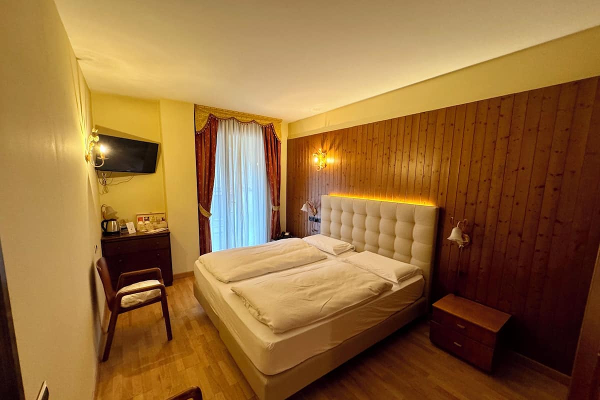 A hotel room with a double bed, wooden paneling on the walls, a desk with a chair, and a television mounted on the wall.