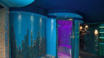 A modern bathroom with blue-tiled walls, a vertical glass panel, and a stone wall with a shelf.