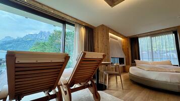 Una habitación de hotel moderna con un ventanal grande, muebles de madera, un sofá y una chimenea.