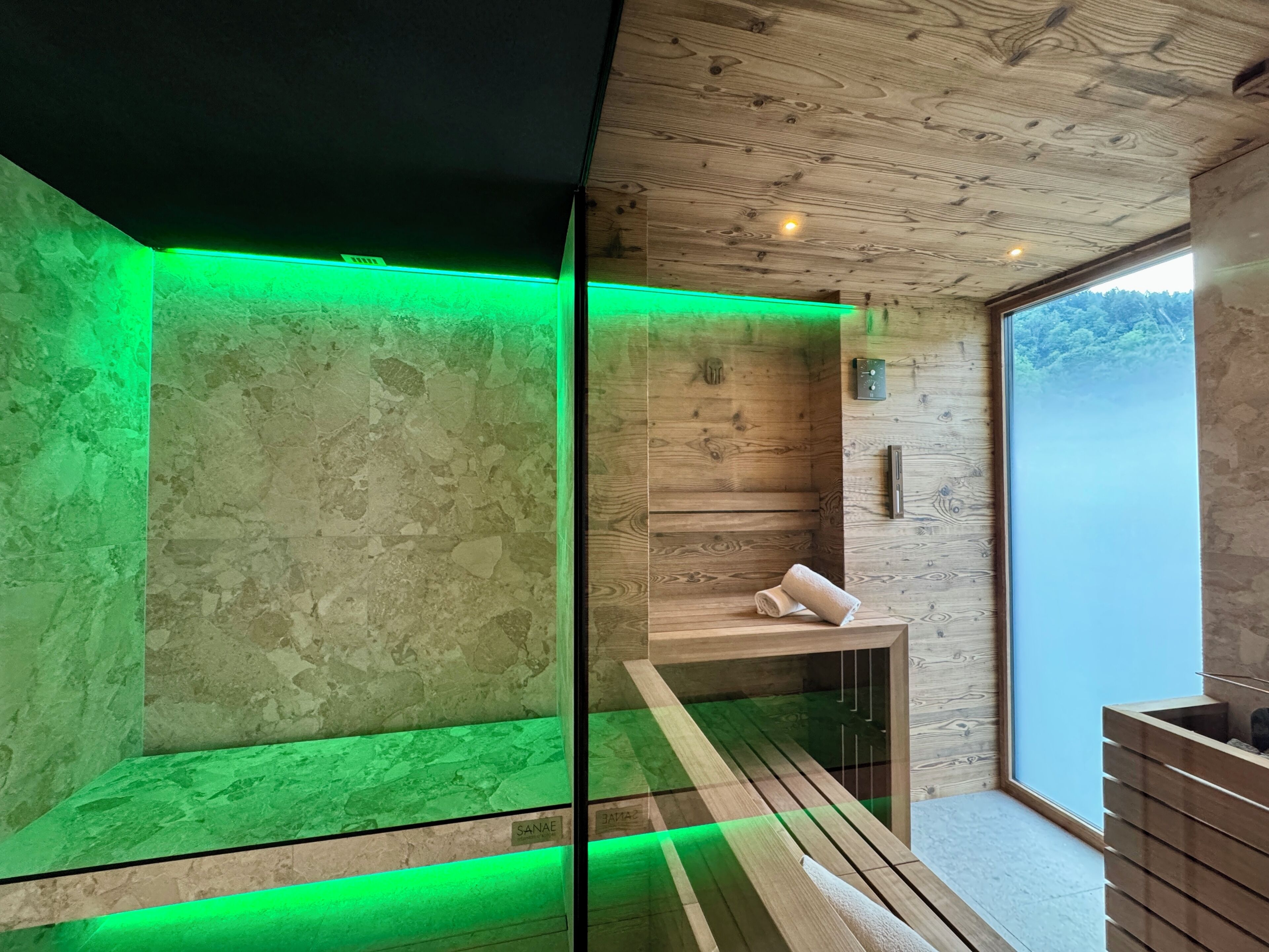 Un bagno moderno con pareti in legno, cabina doccia in vetro e una panca con asciugamani.