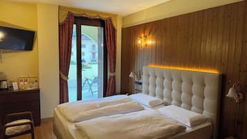 Habitación de hotel con cama, televisor, escritorio con lámpara y vistas al exterior.