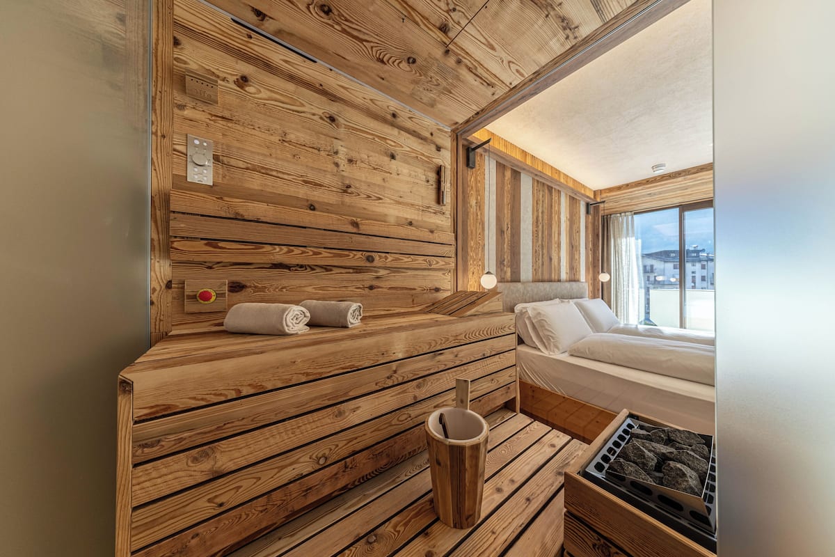 A wooden sauna room with a bench, a small trash bin, and a sauna heater.