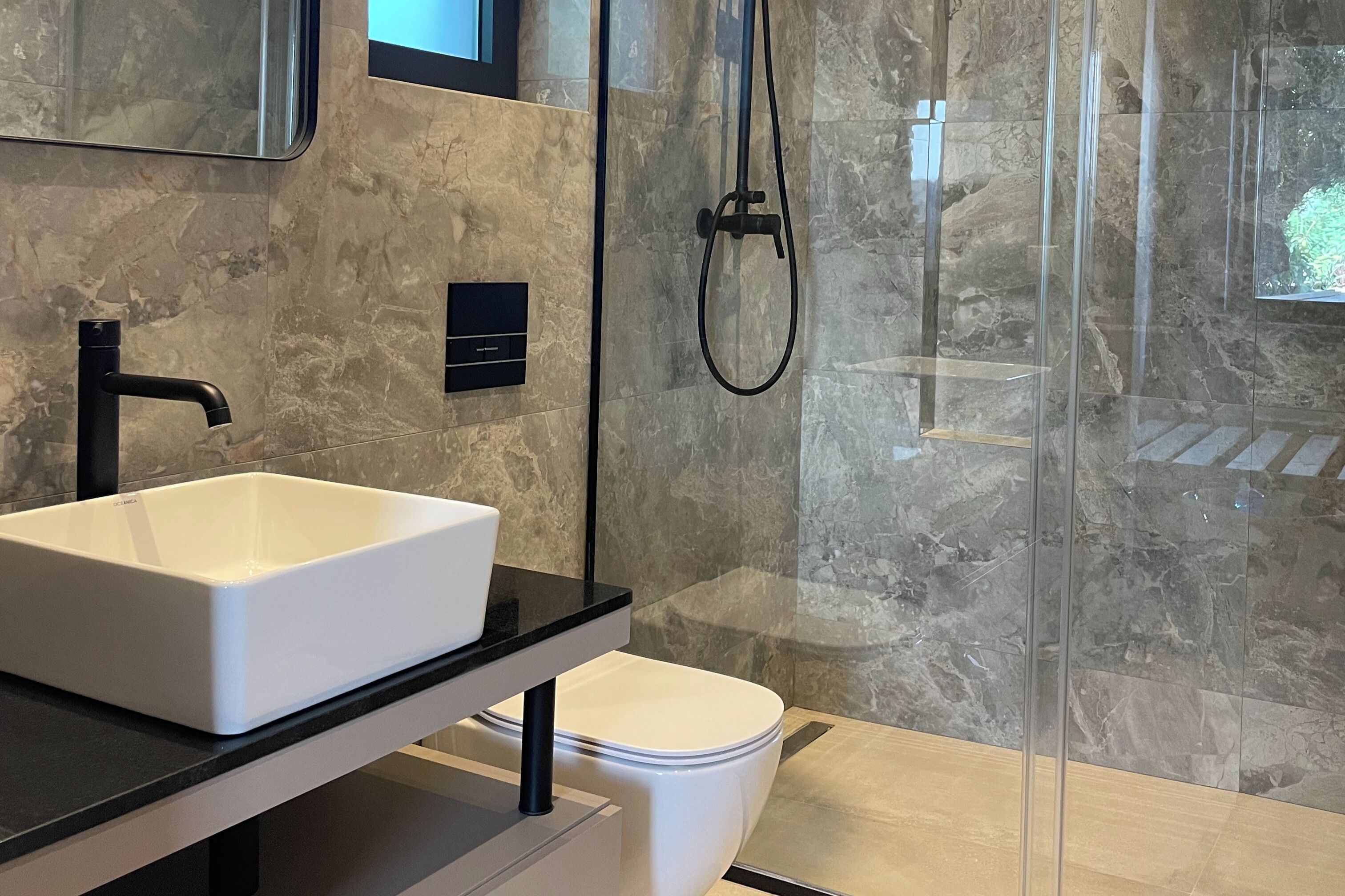 A modern bathroom with a white sink, black faucet, and a glass-enclosed shower.