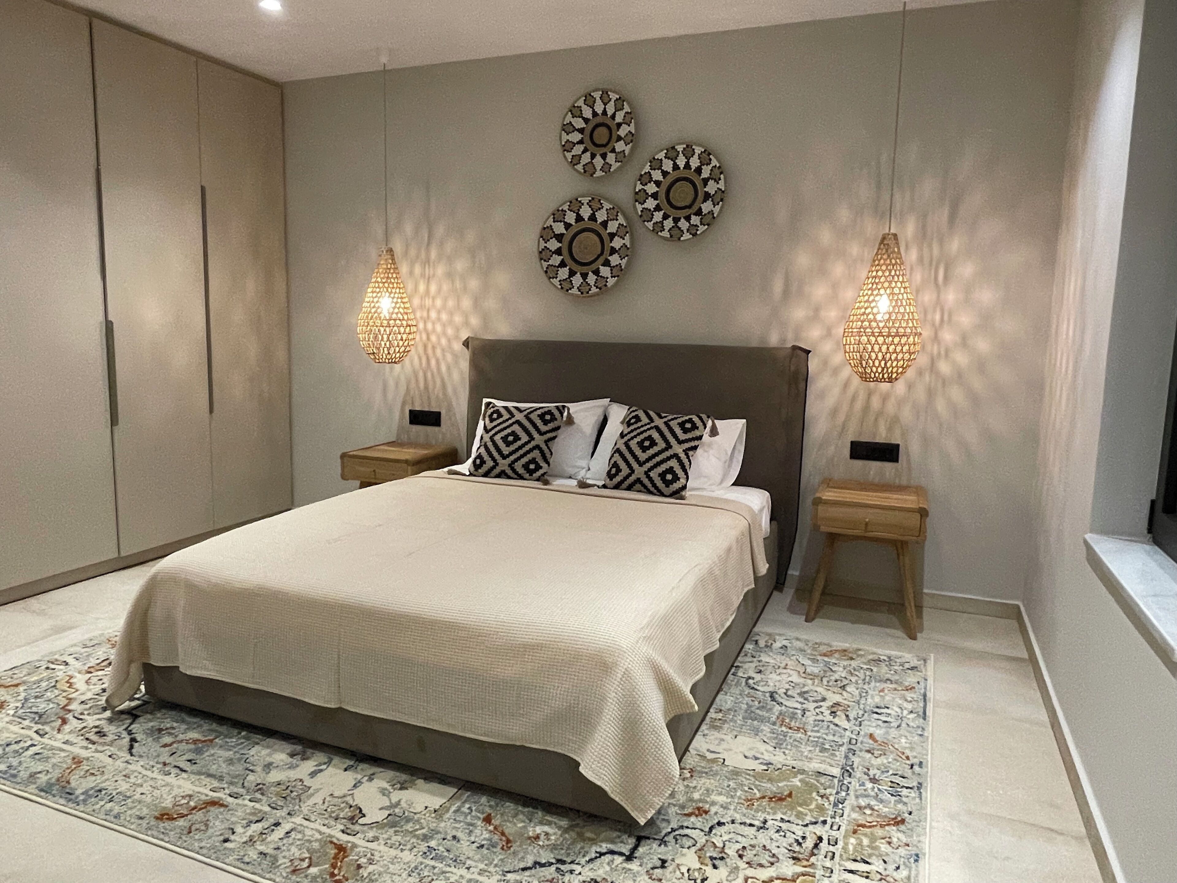 Une chambre à coucher avec un grand lit, deux tables de chevet, un tapis à motifs et des œuvres d’art décoratives accrochées au mur.
