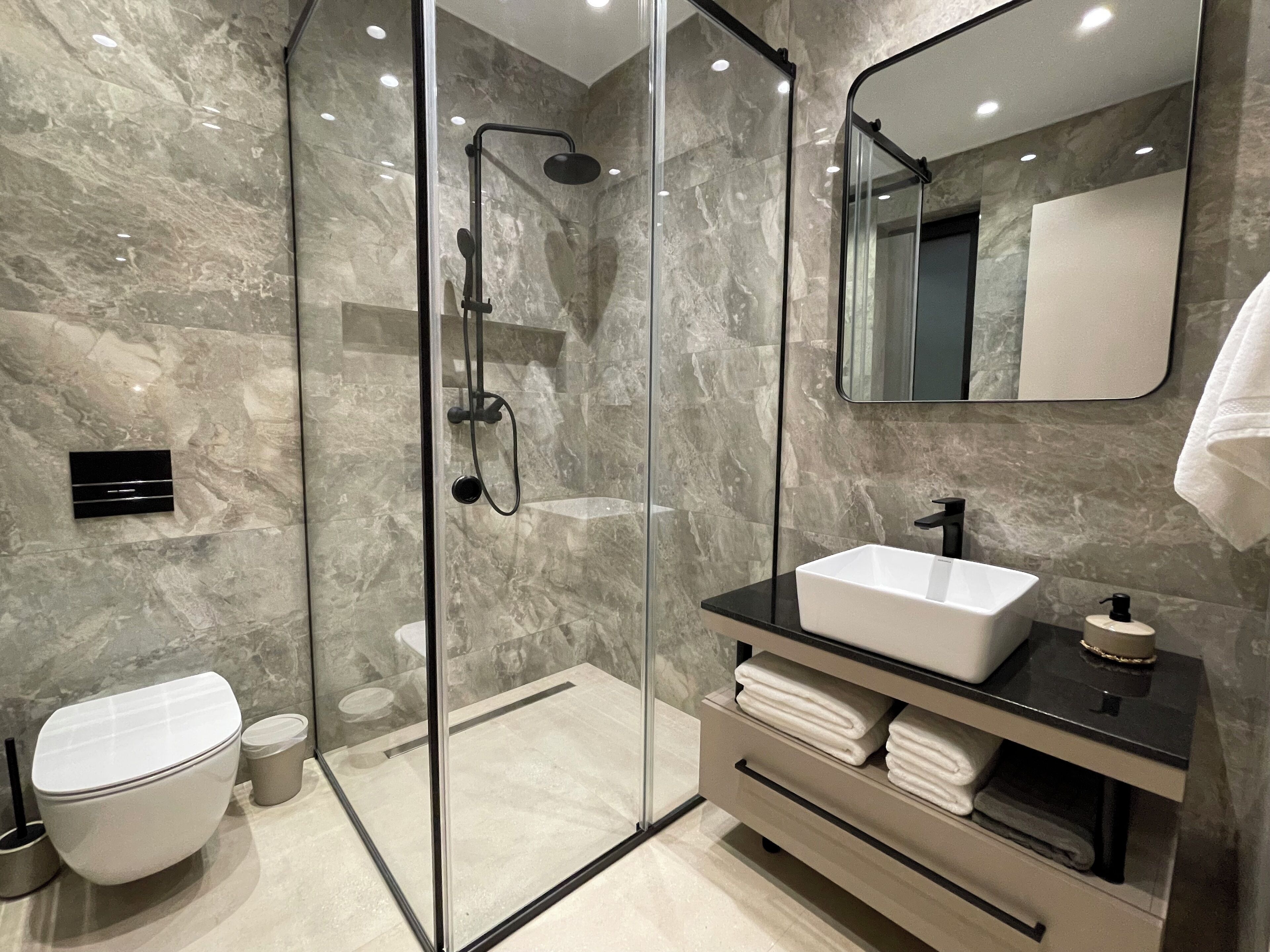 Un baño moderno con ducha de vidrio, lavabo blanco y espejo grande.