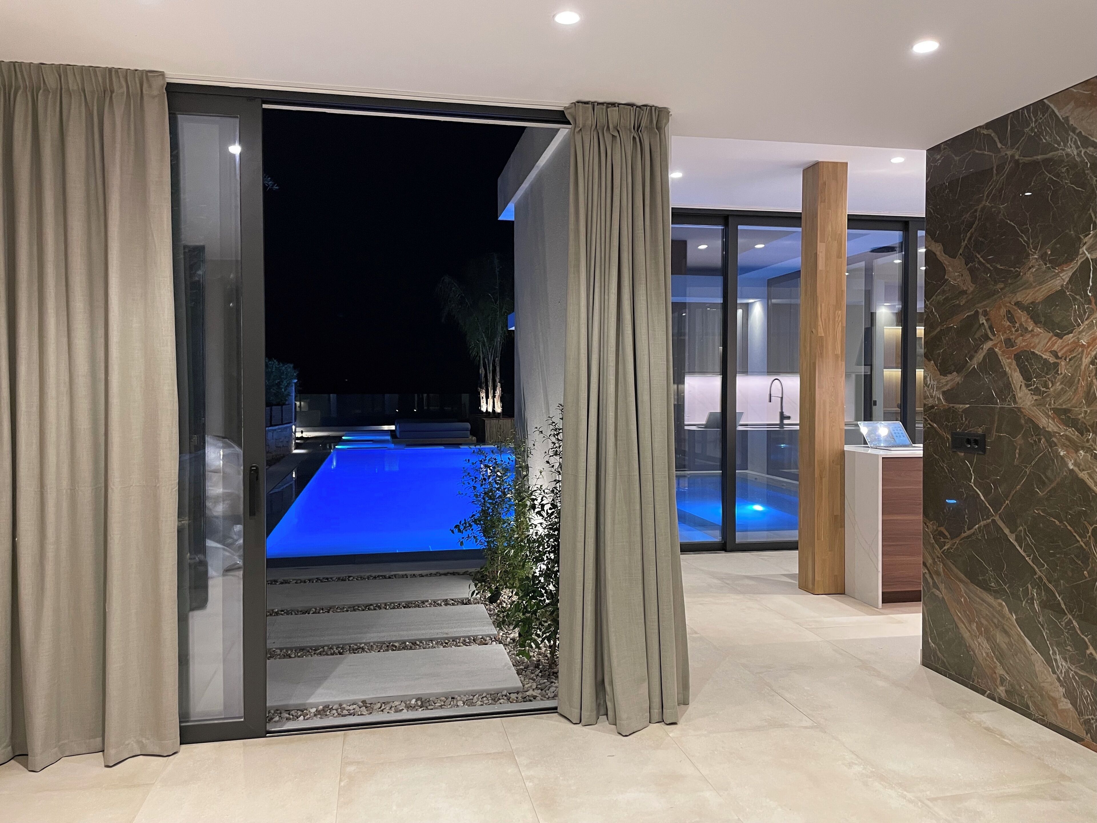 A modern interior with a glass door leading to a pool area, a reception desk, and a stone wall.