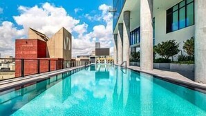 Una piscina en la azotea con agua azul cristalina, rodeada de arquitectura moderna y un cielo despejado.