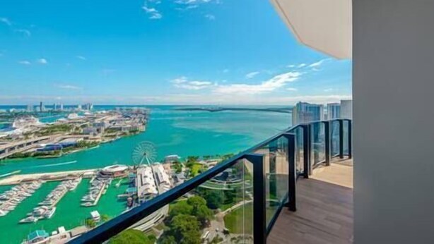 Habitación de hotel en un edificio alto con balcón que da a un puerto deportivo y una noria.