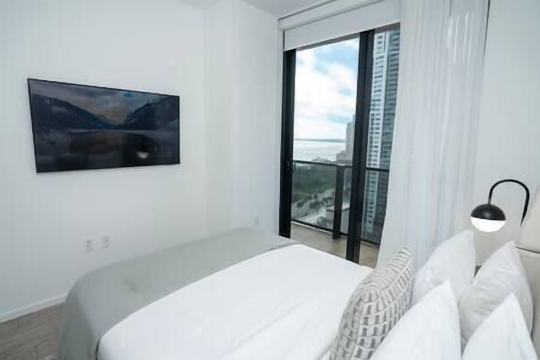 Een hotelkamer met een bed, een raam met uitzicht op gebouwen en een schilderij aan de muur.