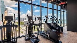 A gym with various exercise equipment, large windows, and a view of a cityscape. - Modern 3BR Oasis in Downtown Miami #1617 (Miami)
