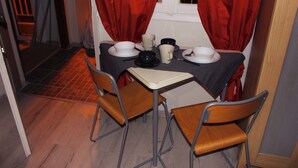 Un coin repas avec une table dressée pour deux personnes, deux chaises et une fenêtre ornée de rideaux rouges.