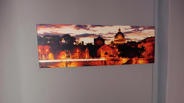 Un canapé gris avec trois coussins, dans une pièce dont le mur est orné d’un tableau représentant un paysage urbain.