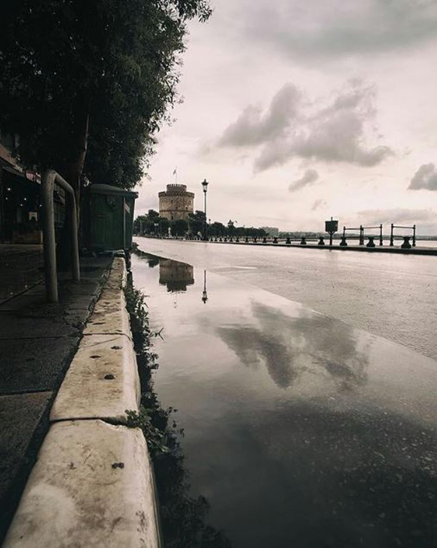 Un paseo marítimo con superficie acuática reflectante, una torre histórica y un muelle distante.