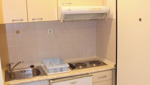 A compact kitchen with white cabinets, a built-in stove, and a small refrigerator. - Studio Sleeps 2 With Free Parking (Thessaloniki)