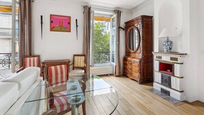 A spacious living room with a glass coffee table, striped armchairs, a wooden cabinet with a mirror, and a fireplace. - Chez Patrick (Paris)