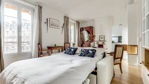 A hotel room with a large bed, a desk, a chair, and a view of the city through the windows. - Chez Patrick (Paris)