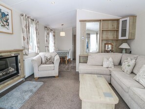 A living room with a fireplace, a sofa, a coffee table, and a dining area with a table and chairs. - Seaviews (Pwllheli)