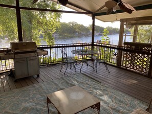 A covered outdoor deck with a grill, a table with chairs, and a view of a lake. - Waterfront Dog-Friendly Lake Home, Cozy Decks and Wood Stove (Burnet)