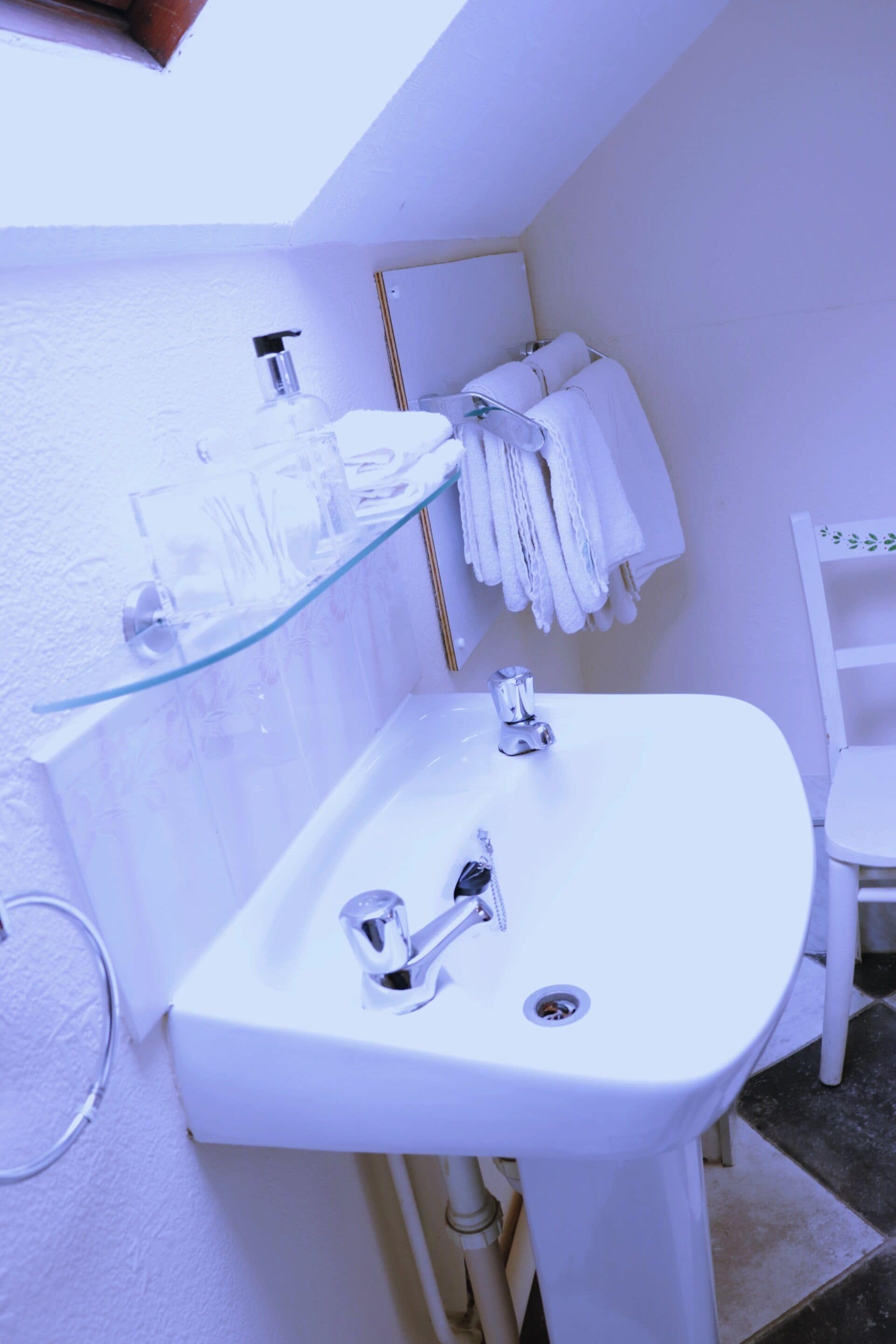 A bathroom with a white sink, glass soap dispenser, and white towels on a rack.
