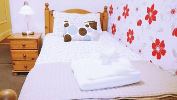 Una cama bien tendida con un papel tapiz estampado con motivos florales y una mesita de noche de madera con una lámpara.