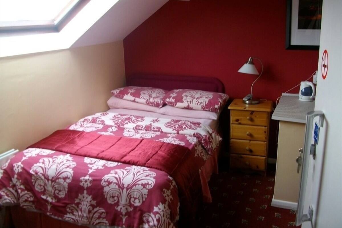 A bedroom with a bed, a nightstand, a lamp, a wardrobe, and a window.