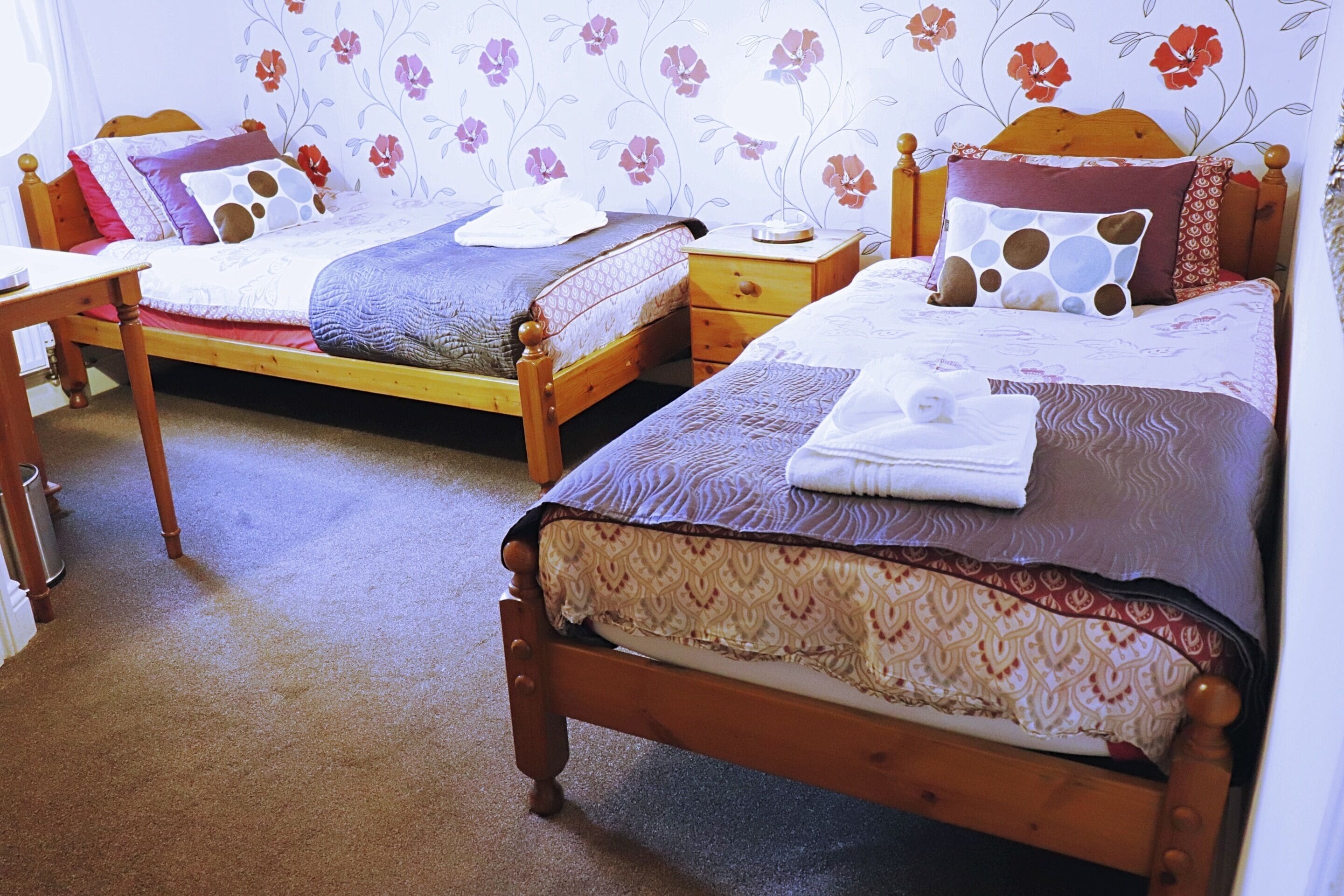 A room with two wooden beds, each with a wooden headboard, a bedside table, and a nightstand.