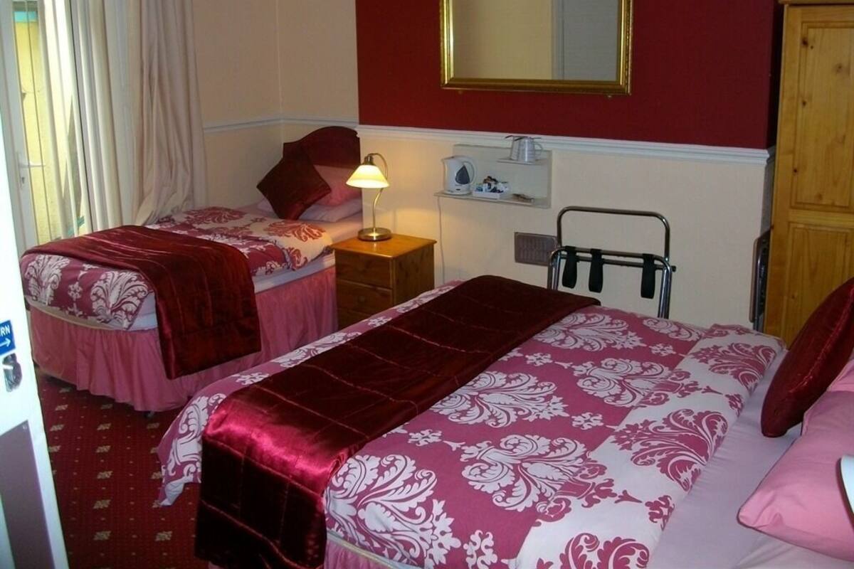 A hotel room with two beds, a mirror, a shelf with toiletries, and a door.