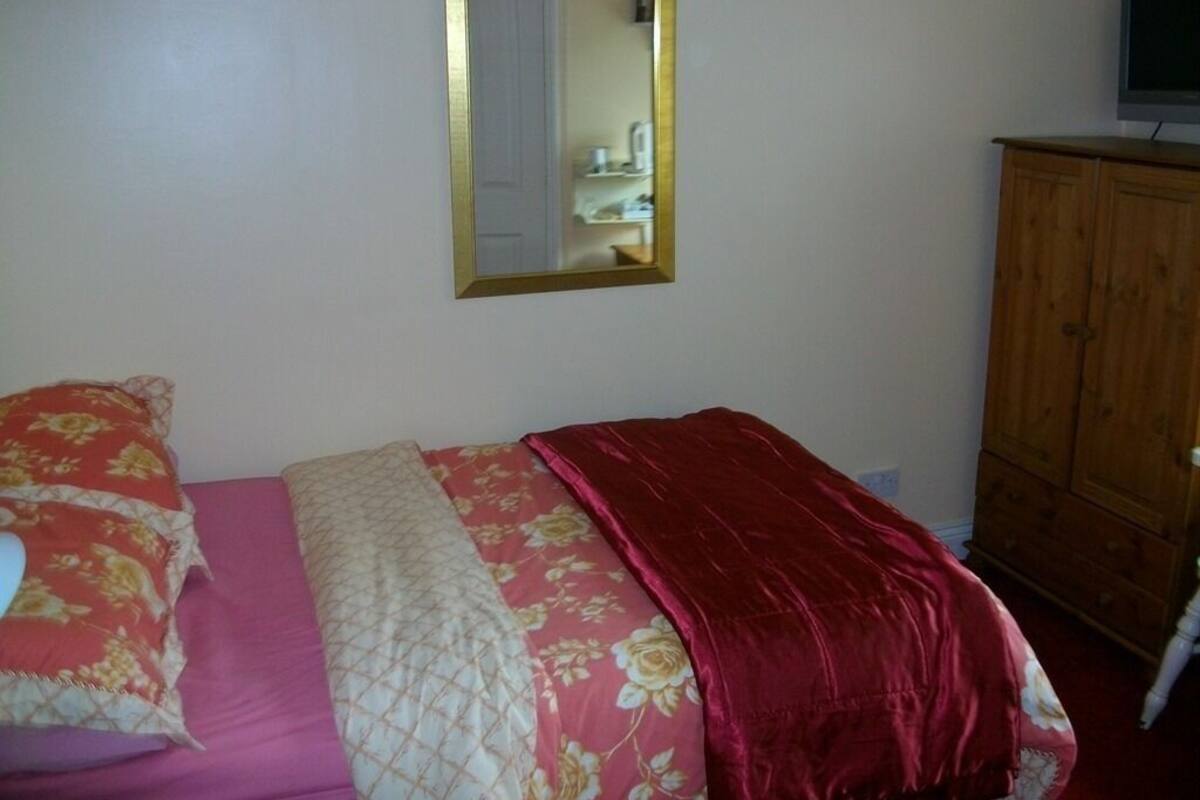 A bedroom with a bed, a mirror, and a wooden wardrobe.